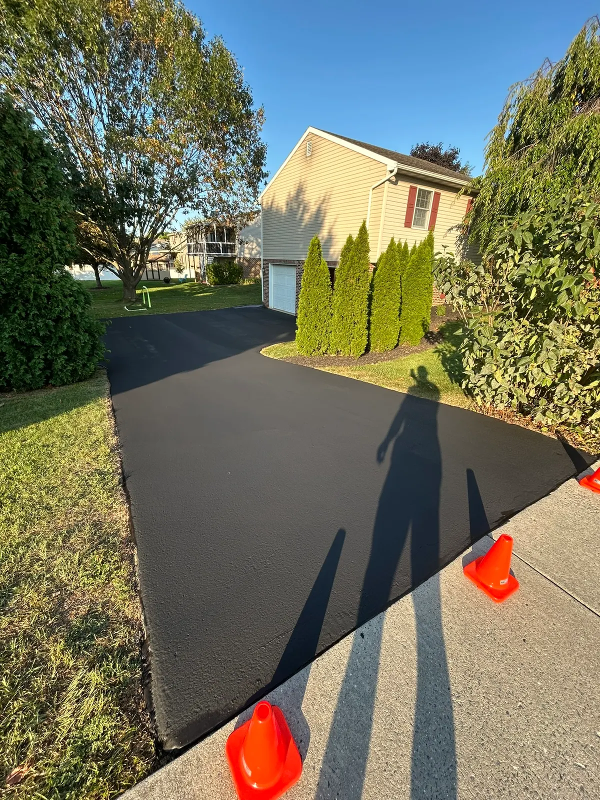 Freshly sealcoated black driveway with orange cones beside a two-story home