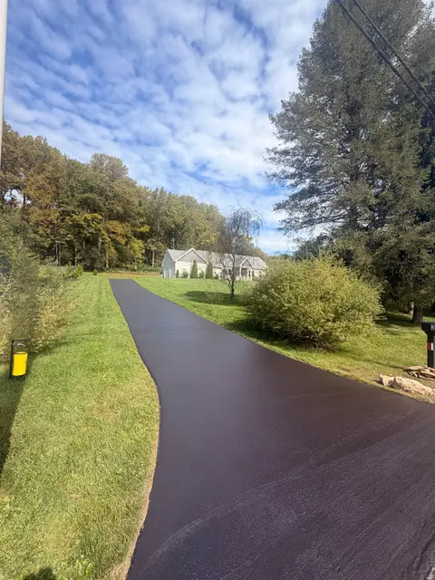 Long sealcoated driveway running toward a house past a tree line